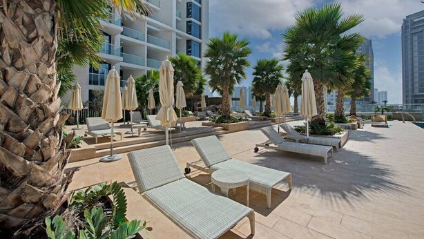 A rooftop pool area with lounge chairs, umbrellas, and palm trees. - BUSINESS BAY - Damac Maison prive, 2907 · Spectacular Burj Khalifa view service apartment (Dubai)