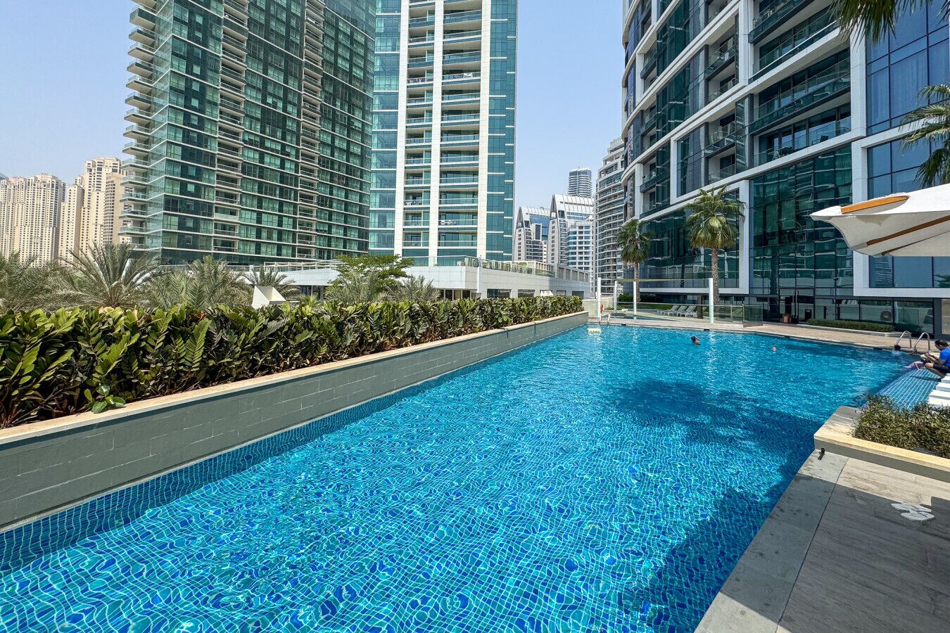 A swimming pool with a tiled edge, surrounded by modern buildings and greenery.