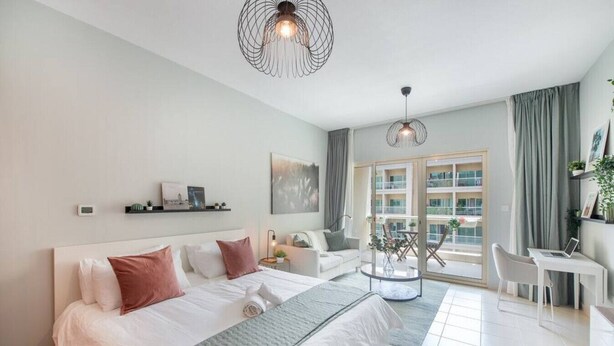 A modern hotel room with a large bed, a desk, and a balcony with a view.
