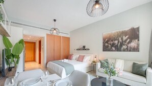 A modern hotel room with a bed, a sofa, a dining table set for two, and a large window.