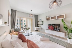 A modern hotel room with a bed, a desk, a chair, a TV, and a balcony with a view of the city.
