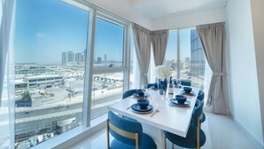 Comedor con vistas a la ciudad, una mesa blanca, sillas azules y un jarrón con flores.