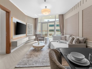 A modern living room with a flat-screen TV, a round coffee table, a sofa, and a dining table with plates.