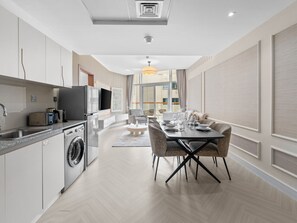 A modern kitchen with a washing machine, a dining area with a table and chairs, and a large window.