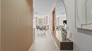 Un corredor moderno de hotel con un revestimiento de paneles de madera, una zona de comedor con una mesa y sillas, y un florero con flores sobre una encimera.