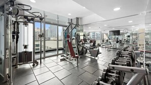 A modern gym with various exercise equipment, large windows, and a city view. - Classic Studio With Dubai Marina View (Dubai)