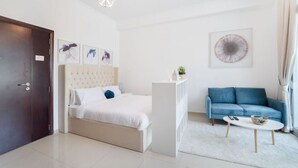 A modern hotel room with a bed, a blue sofa, a white coffee table, and a white cabinet. - Classic Studio With Dubai Marina View (Dubai)