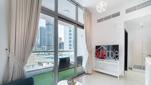 A modern living room with a large window, a sofa, a small table with a bowl, and a TV displaying 'suiteable' on the wall. - Classic Studio With Dubai Marina View (Dubai)