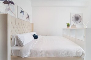 A modern bedroom with a tufted headboard, white bedding, and minimalist decor.