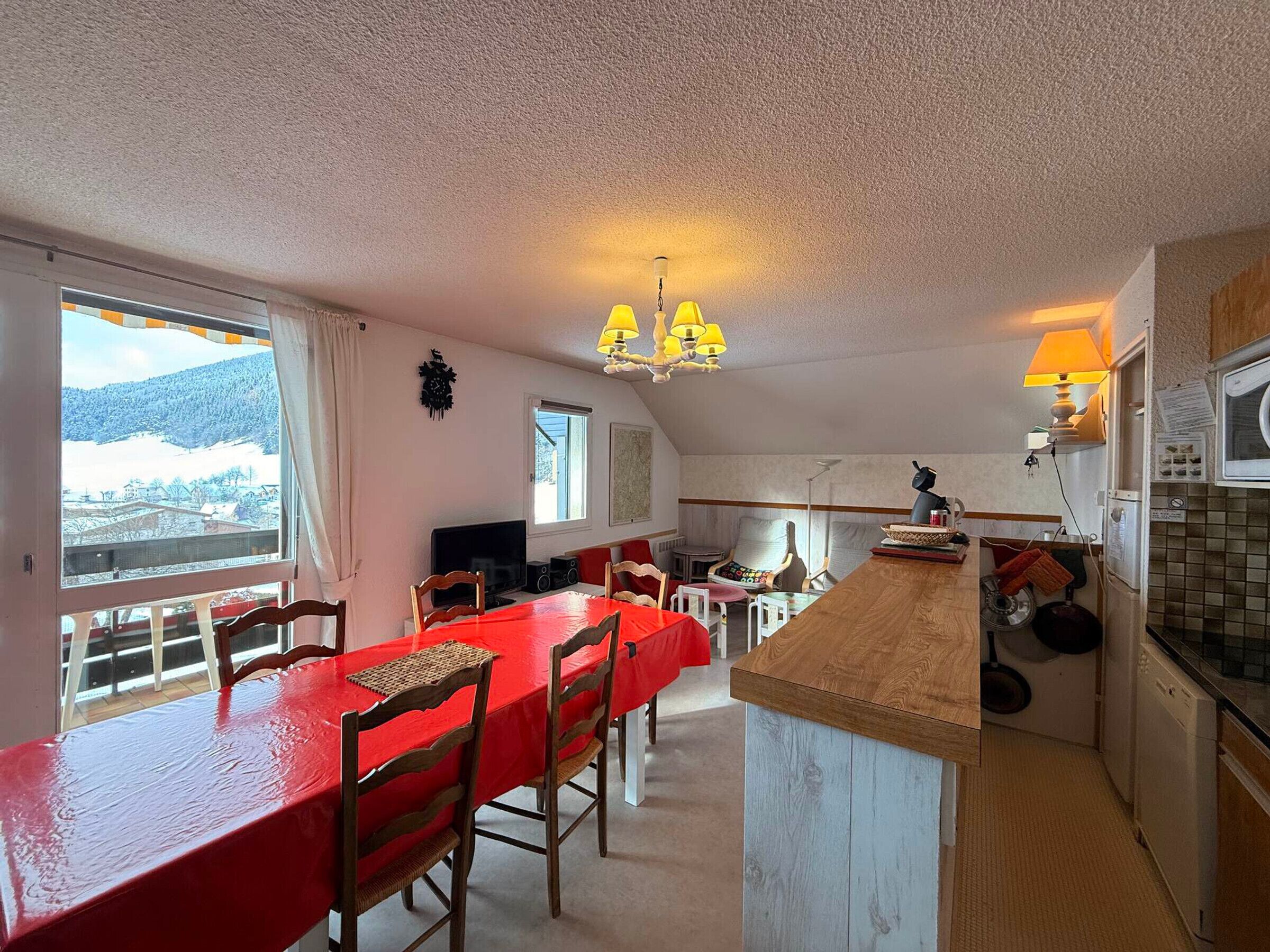 A cozy kitchen with a wooden island, a dining table with chairs, and a view of a snowy landscape through the windows.