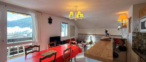 A cozy kitchen with a wooden island, a dining table with chairs, and a view of a snowy landscape through the windows.