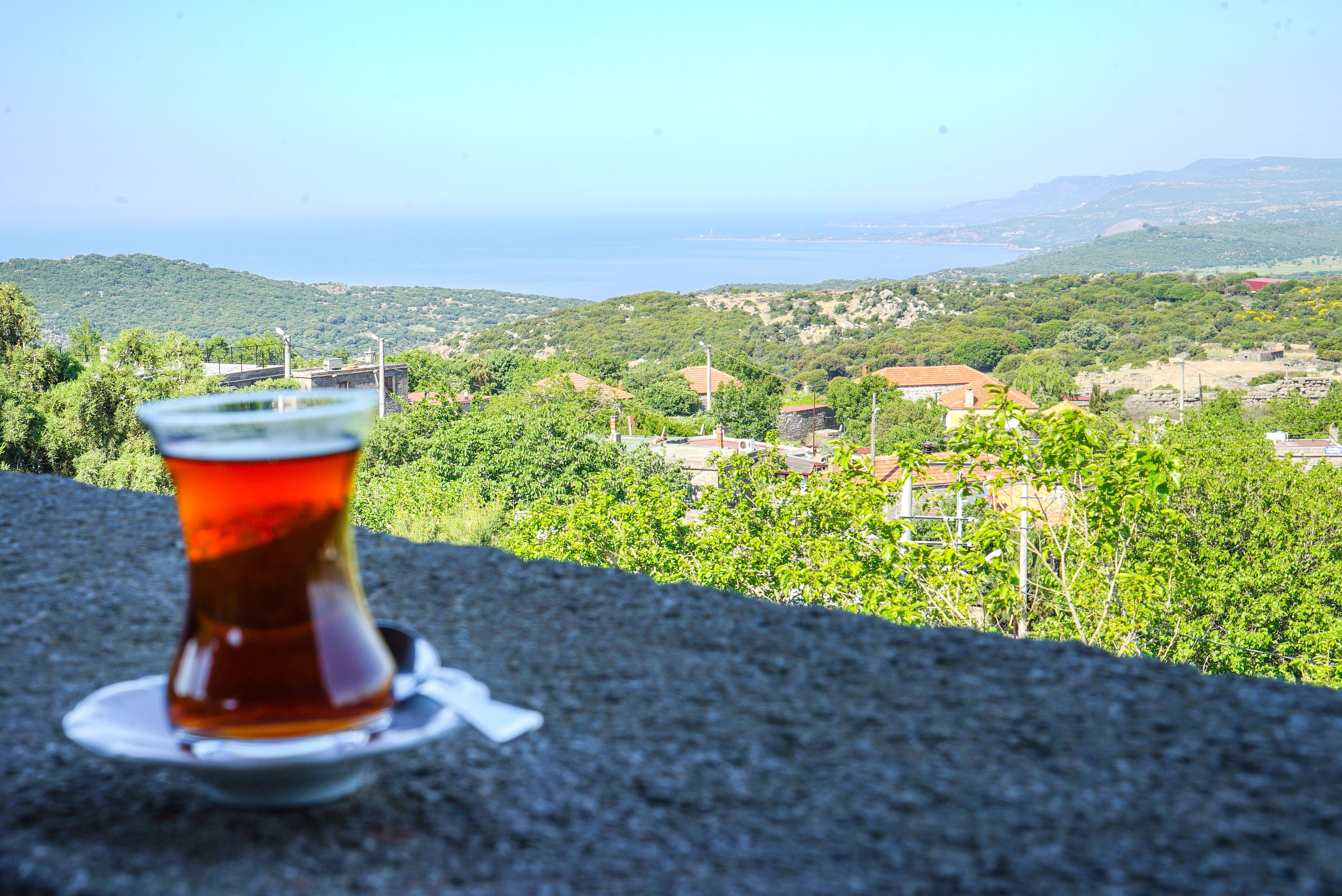 A glass of tea on a stone ledge with a view of a coastal landscape.