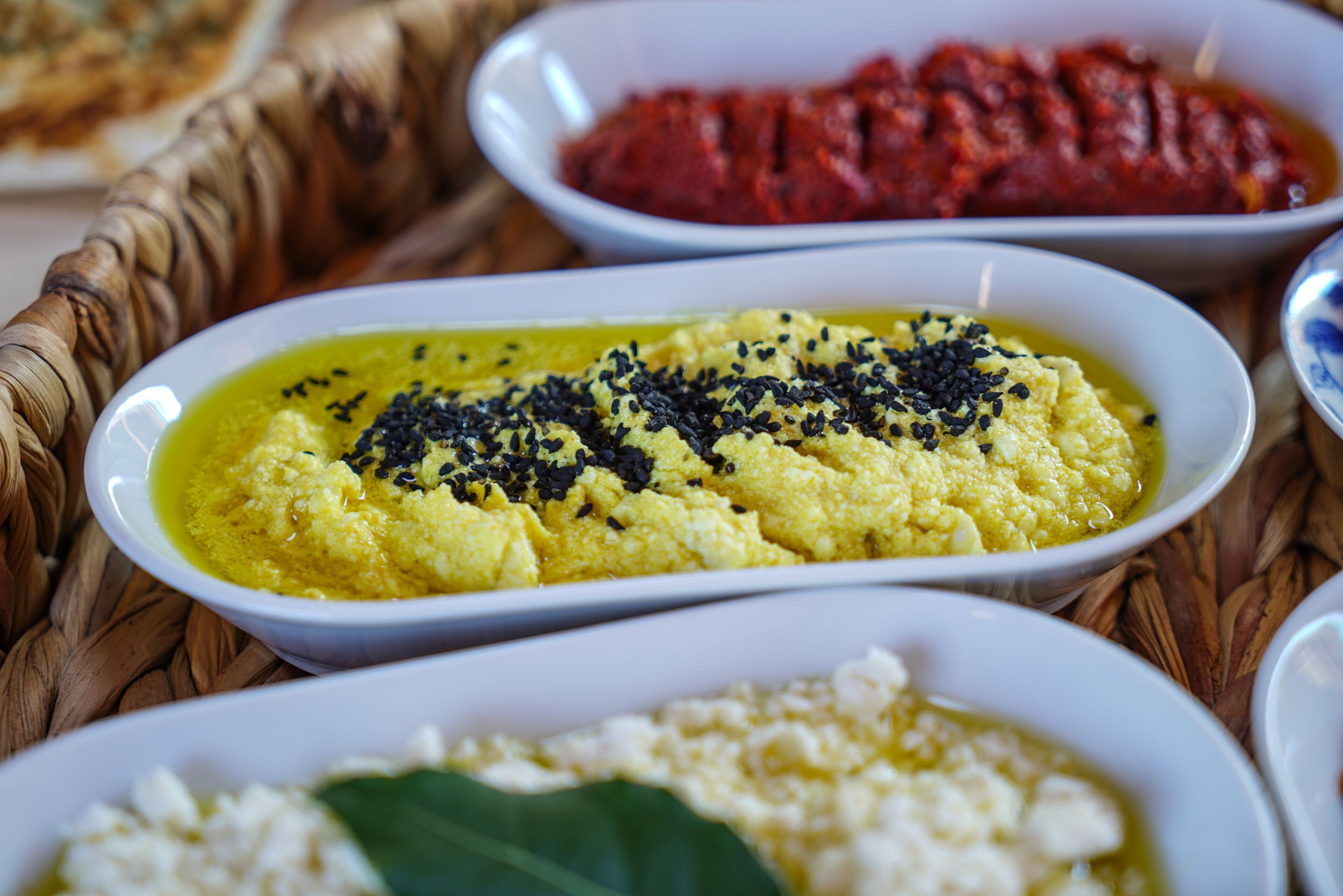 A variety of dishes on a table, including a yellow dish with black seeds, a red dish, and a white dish with a green leaf.