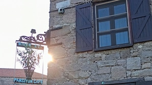 Um edifício de pedra com uma placa indicando 'Pansiyon Cafe' e um carro estacionado.