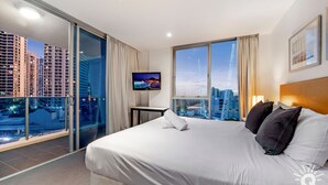 A hotel room with a large bed, a TV, a balcony with a city view, and a large window. - H'Residences – 2 Bedroom 1 Bathroom, Ocean View (Surfers Paradise)