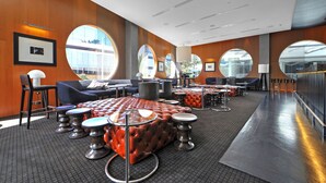 A modern hotel lobby with leather seating, round tables, and large windows offering views of the city. - H'Residences – 2 Bedroom 1 Bathroom, Ocean View (Surfers Paradise)