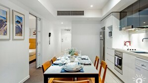 A modern kitchen with a dining area, white walls, and a large window. - H'Residences – 2 Bedroom 1 Bathroom, Ocean View (Surfers Paradise)