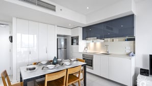 A modern kitchen with white cabinets, stainless steel appliances, and a dining table set for four. - H'Residences – Cozy 2 Bed Hinterland View — Q Stay (Surfers Paradise)