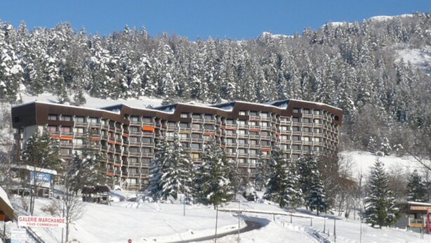 Ein mehrgeschossiges Hotel mit modernem architektonischen Design, umgeben von schneebedeckten Bäumen und einer Bergkulisse.