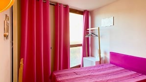 Ein Zimmer mit einem Bett, einem Vorhangfenster, einem Kleiderschrank und einem kleinen Tisch.