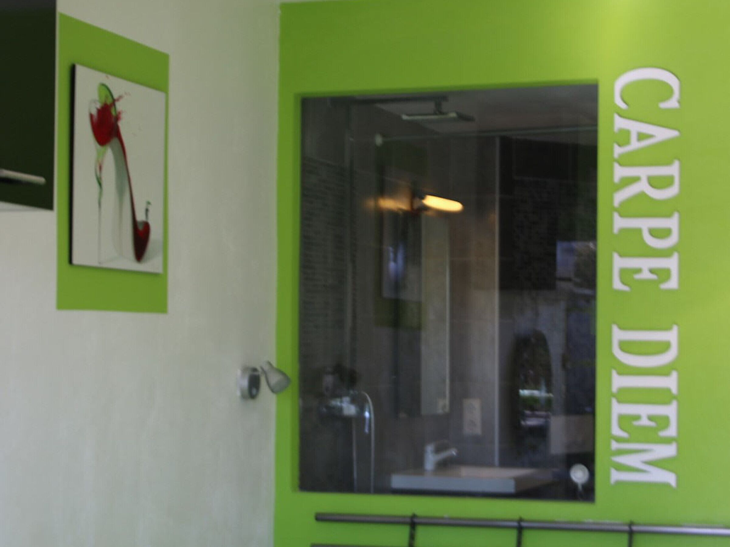 A bathroom with a green accent wall, a framed artwork, and a large window with a sink and mirror.