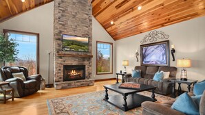 Un salón amplio con chimenea de piedra, asientos cómodos y ventanas grandes con vistas al exterior.