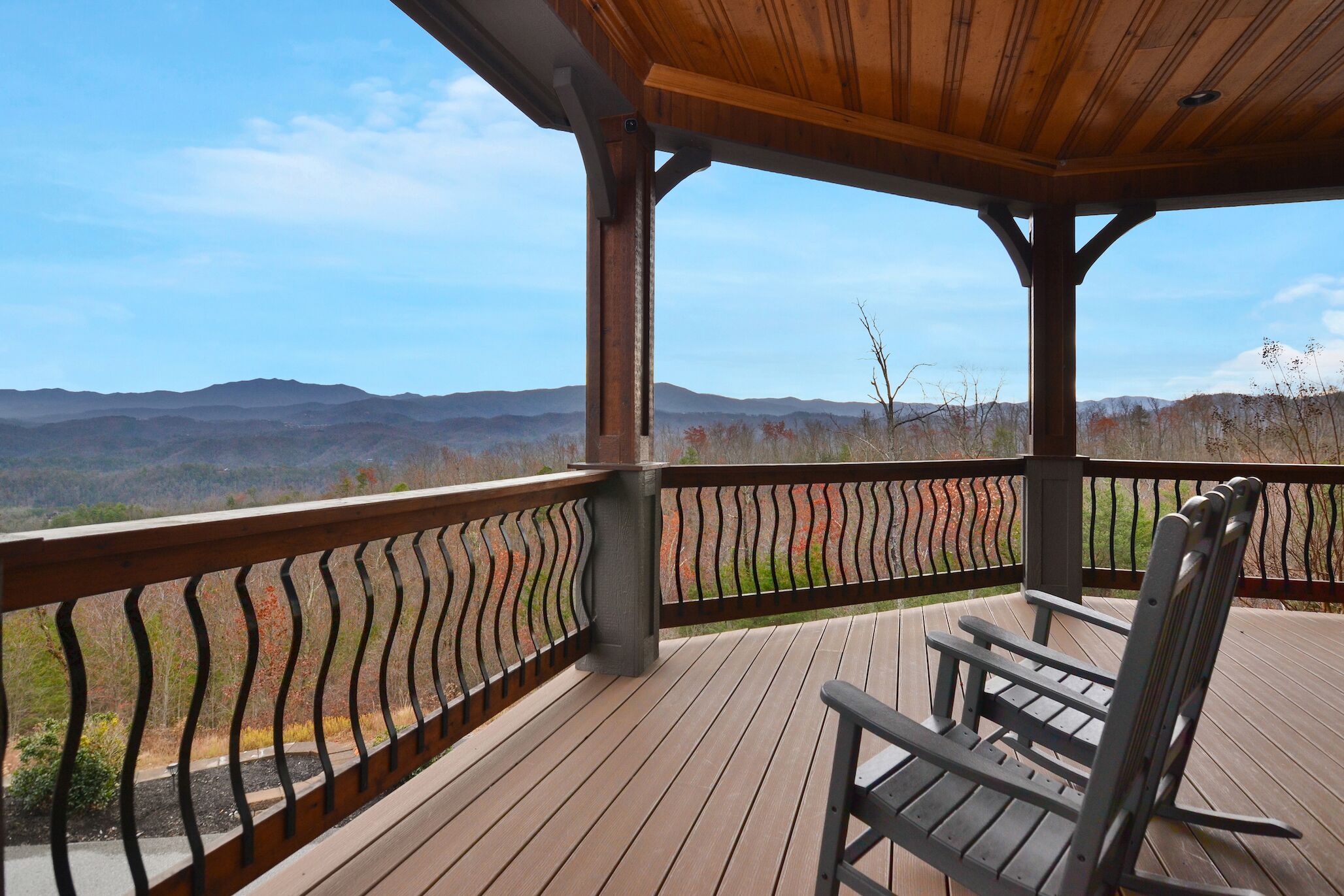 A covered deck with a wooden railing, a bench, and a view of distant mountains.