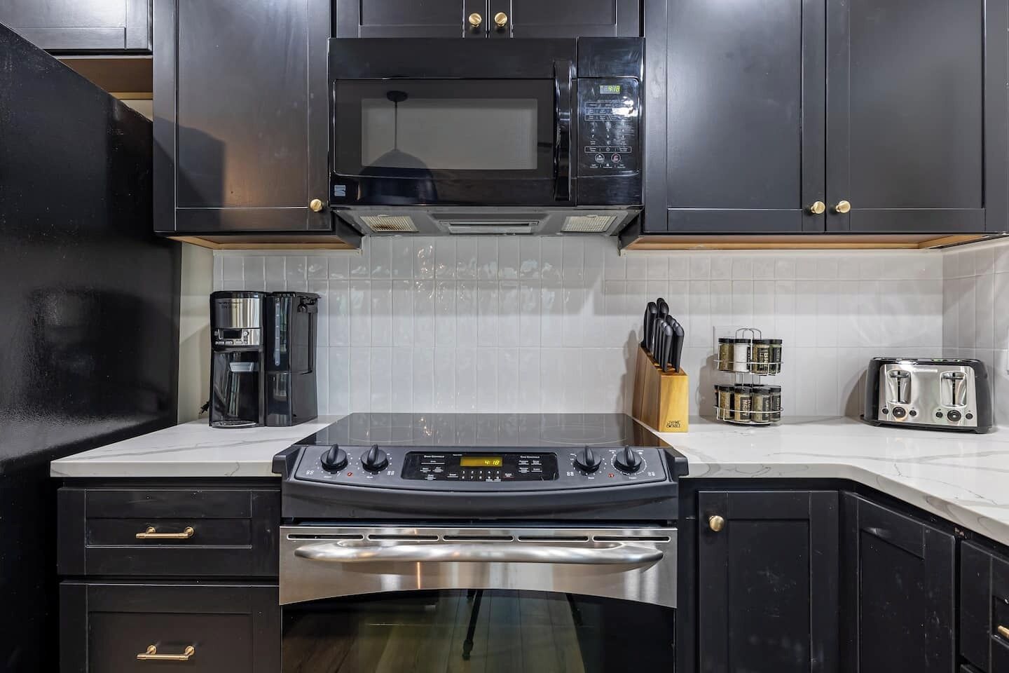A modern kitchen with dark cabinetry, a stainless steel stove, a microwave, a coffee maker, a toaster, and a knife block.
