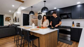 A modern kitchen with a central island, black cabinets, and stainless steel appliances.