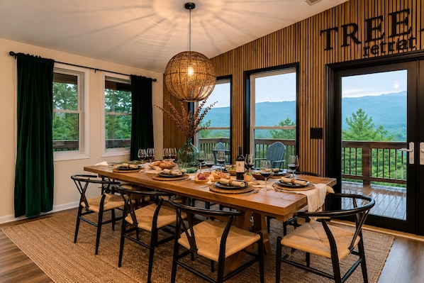 Comedor con una mesa de madera dispuesta para una comida, ventanas amplias y vistas al exterior.