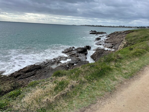 A coastal landscape with rocky terrain and a dirt path alongside the sea.