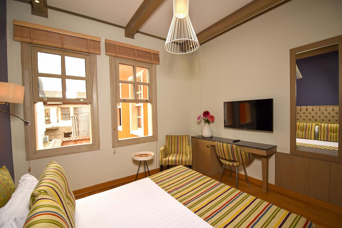 A hotel room with a bed, a desk, a TV, and a window with blinds.