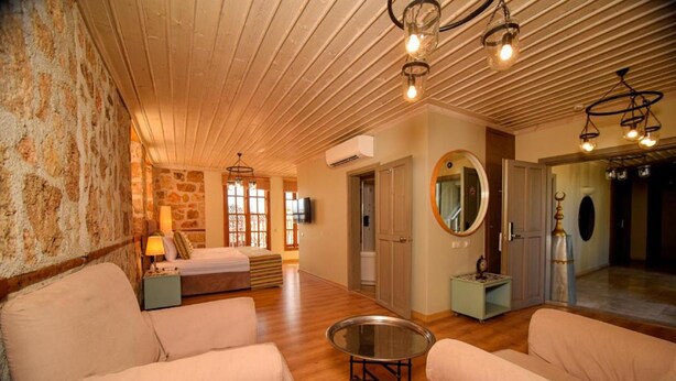 Una habitación acogedora con pared de piedra, techo de madera y un espejo redondo. Hay dos sofás color beige y una pequeña mesa redonda.