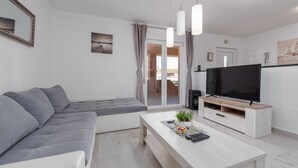 A modern living room with a grey sectional sofa, a white coffee table with decorative items, a flat-screen TV on a wooden stand, and a sliding glass door leading to an outdoor area. - Villa Jenny, private pool, 4+1, peace and quiet, BBQ (Murvica)