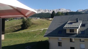 Un edificio con techo inclinado, vista a un paisaje montañoso y un campo cubierto de césped con un sendero.