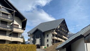 Un edificio moderno de varios pisos con balcones, un camino de entrada curvo y un paisaje nevado al fondo.