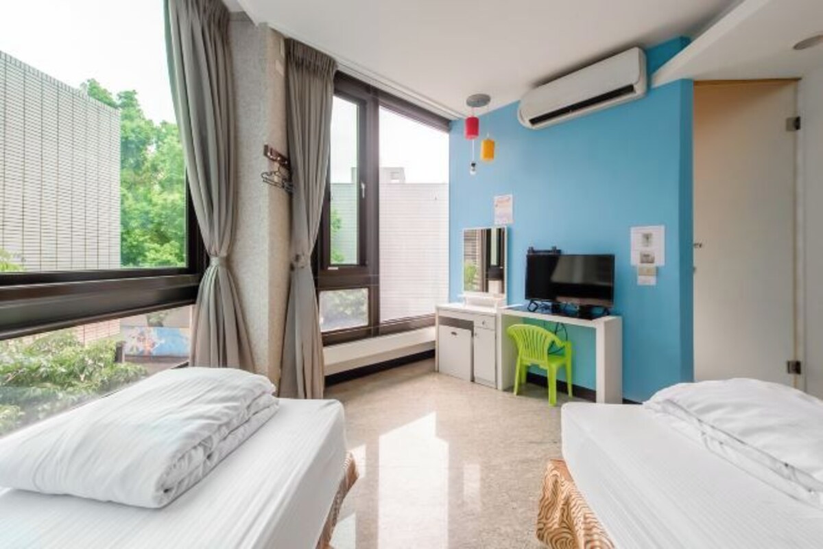 Habitació d'hotel amb dos llits, un escriptori amb cadira, televisió i aire condicionat.