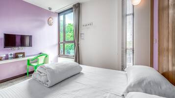 A hotel room with a bed, a desk with a computer, a TV, and a window with curtains.