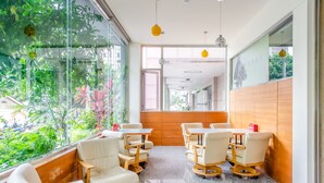 A modern indoor space with a seating area featuring cushioned chairs and tables, large windows with a view of greenery, and a wooden accent wall. - Lightness Hotel (Tainan)