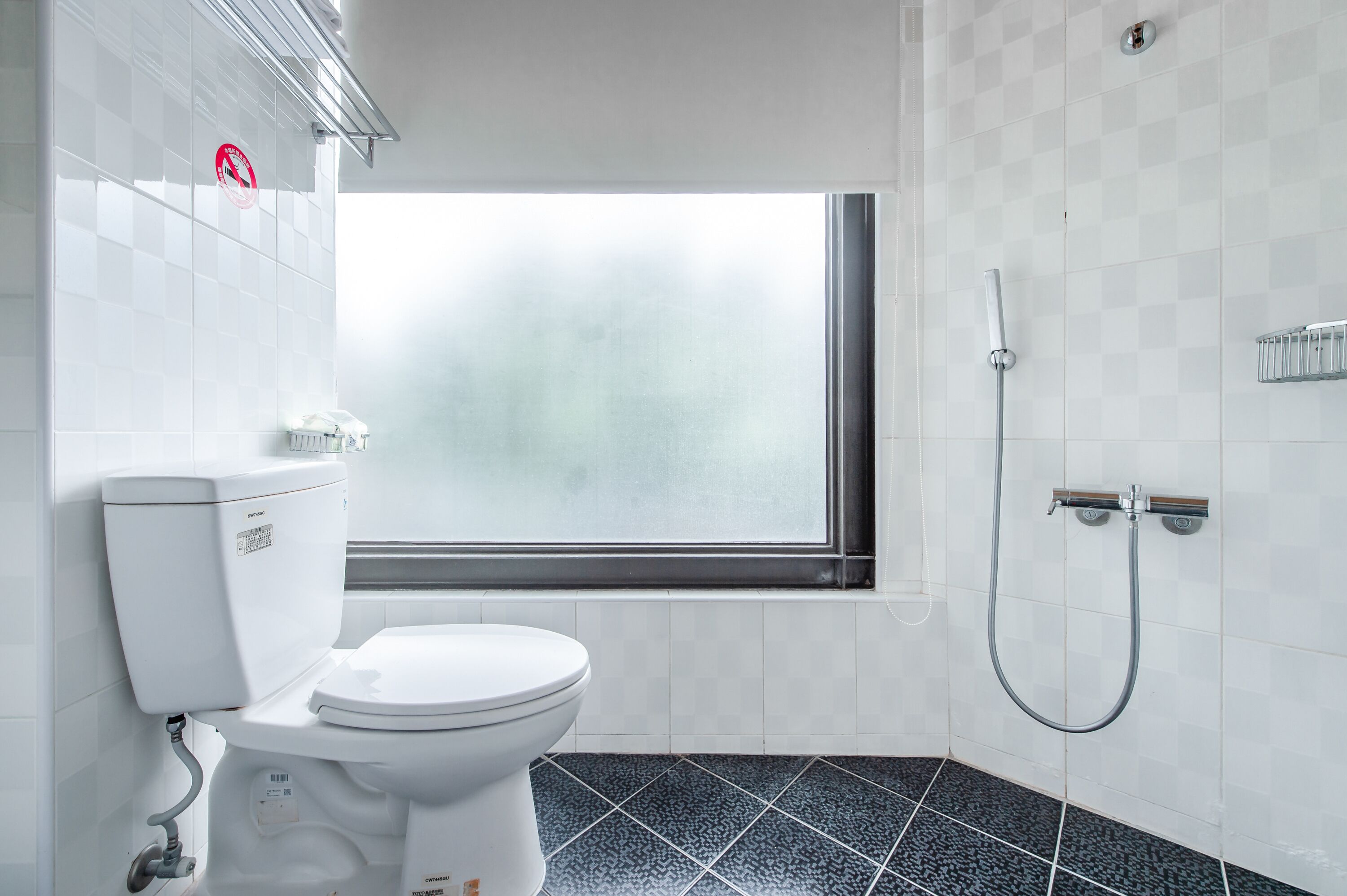 A bathroom with a toilet, a window, and a shower.