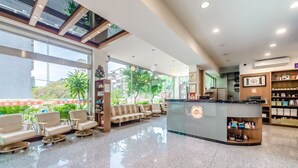 A modern hotel lobby with a reception desk, seating area, and large windows offering views of greenery and buildings. - Lightness Hotel (Tainan)