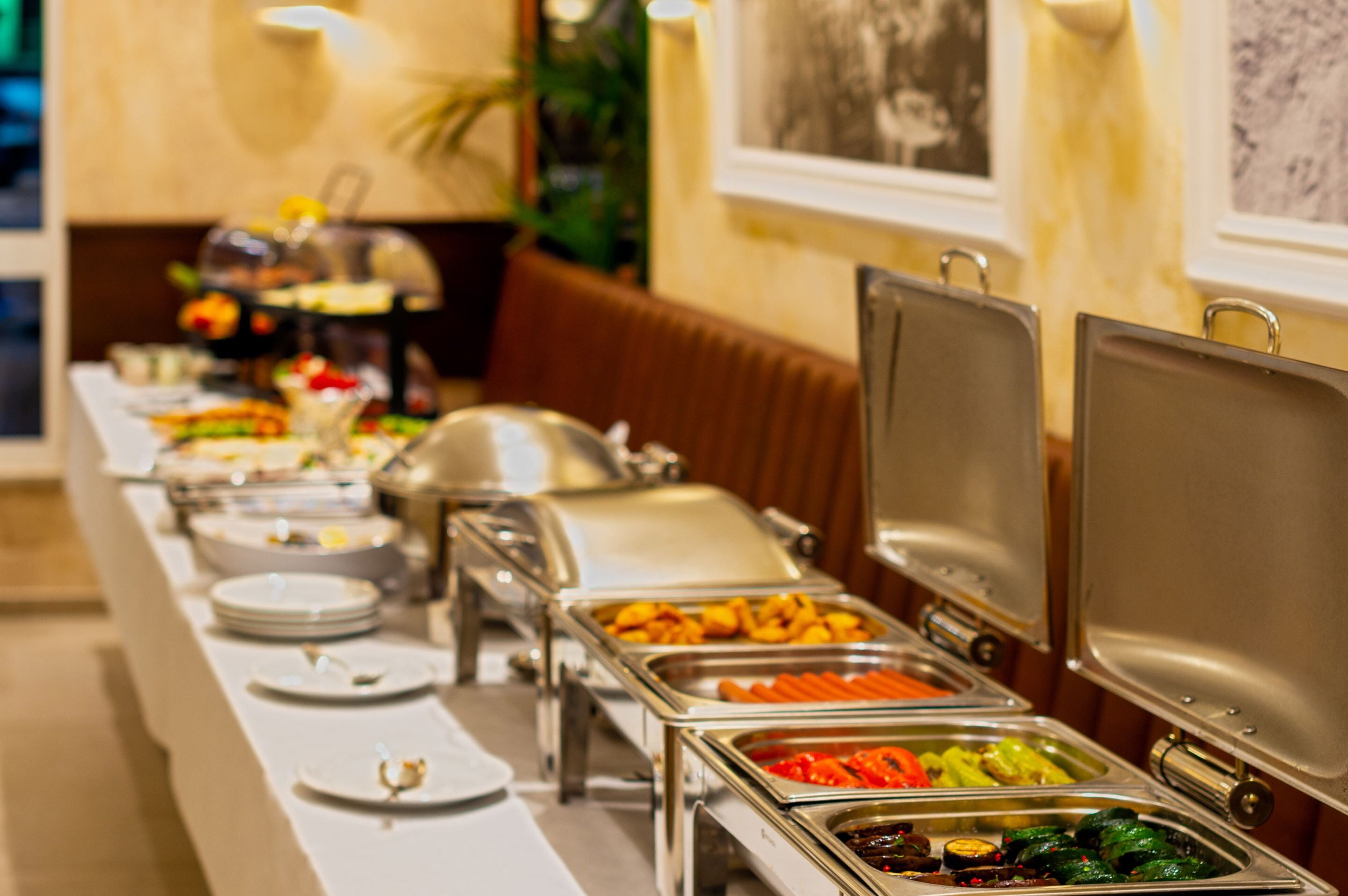 A buffet setup with various food items in metal containers, arranged on a long table with plates and cutlery.