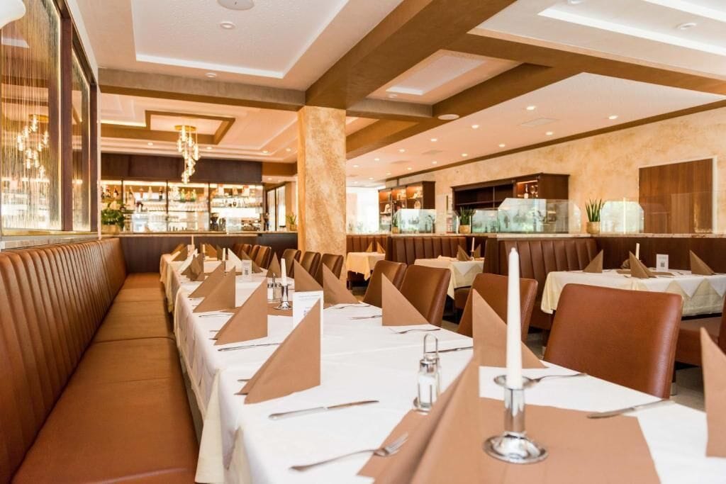 Un restaurant avec de longues tables dressées pour le service, un bar et un espace détente avec des bancs rembourrés.
