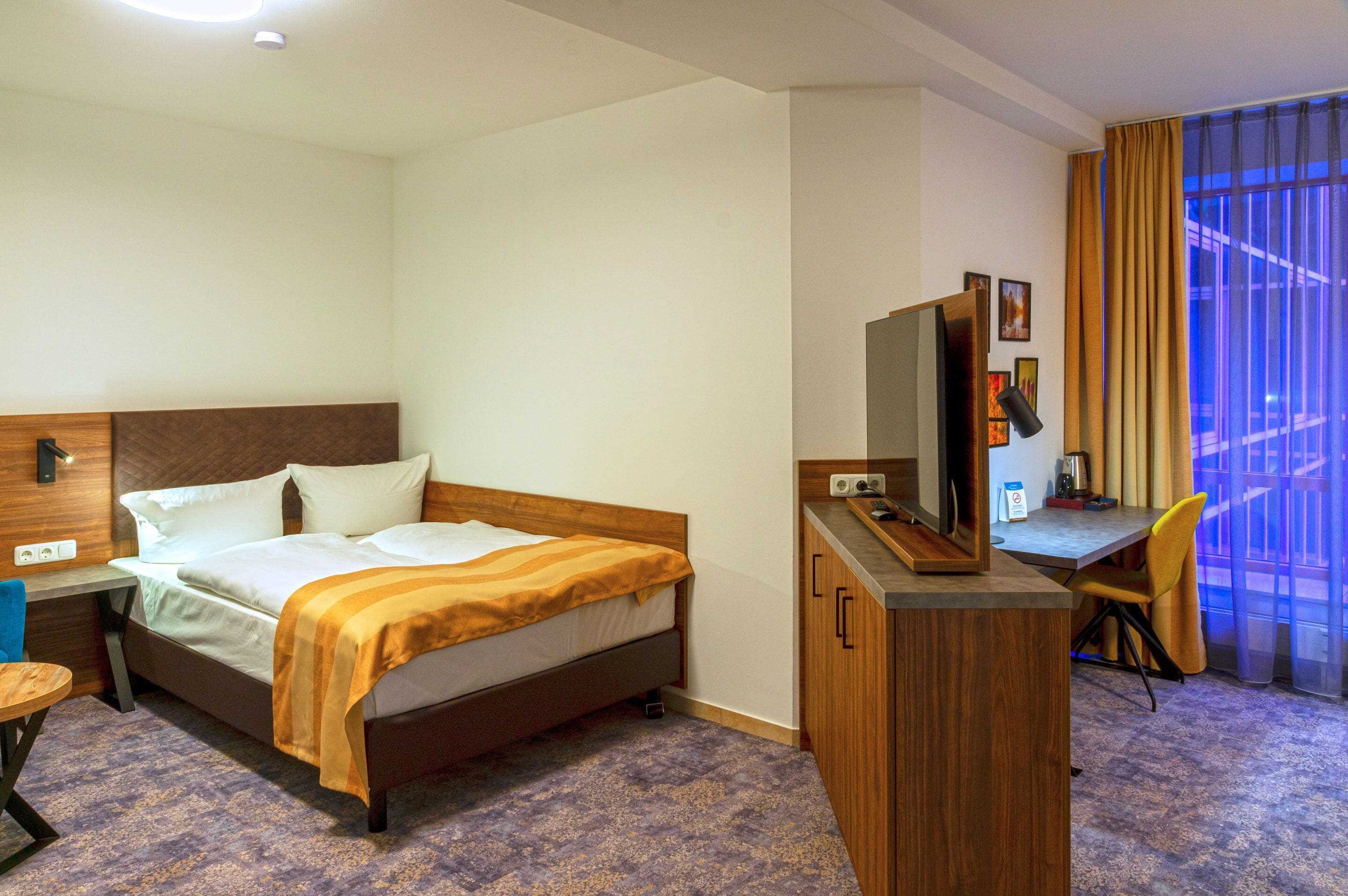 Een hotelkamer met een bed, een bureau, een stoel, een televisie en een raam met gordijnen.