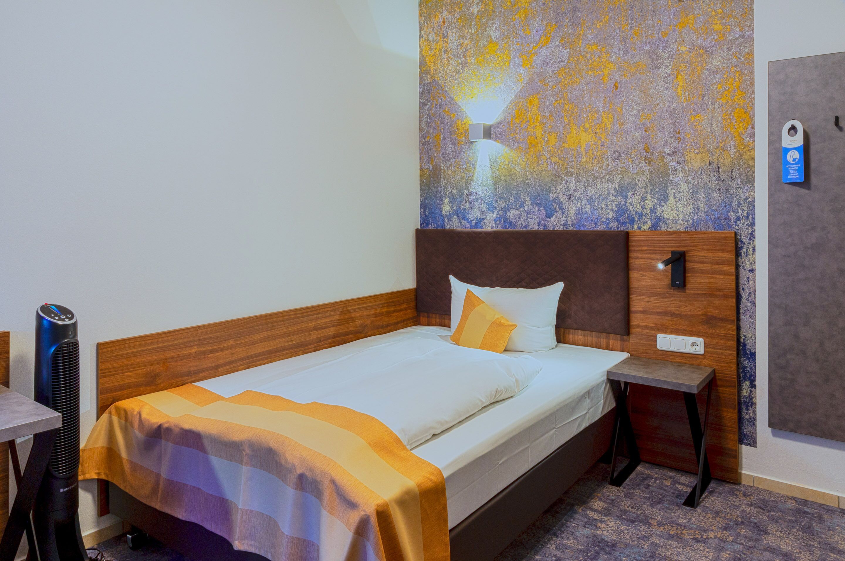 Hotelkamer met een bed, nachtkastje, wandairconditioner en een deur met slot.