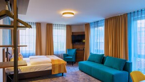 Quarto de hotel com cama, sofá, escrivaninha e televisão.