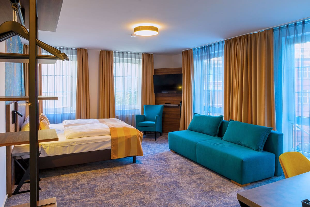 A hotel room with a bed, a sofa, a desk, and a television.
