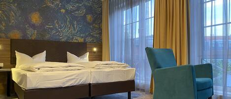 Een hotelkamer met een groot bed, een groene fauteuil en een muur met een abstract schilderij in blauw en geel.