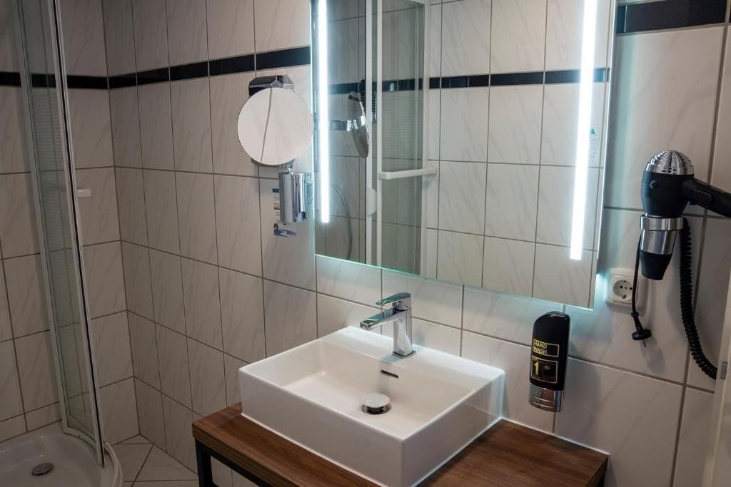 A modern bathroom with a white sink, a handheld showerhead, and a mirror with a round mirror above it.