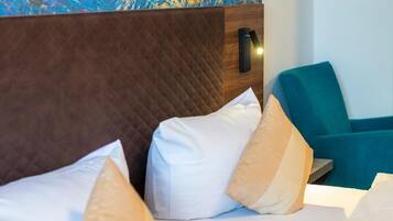 Habitación de hotel con cabecera acolchada, un sillón verde azulado y ropa de cama blanca.